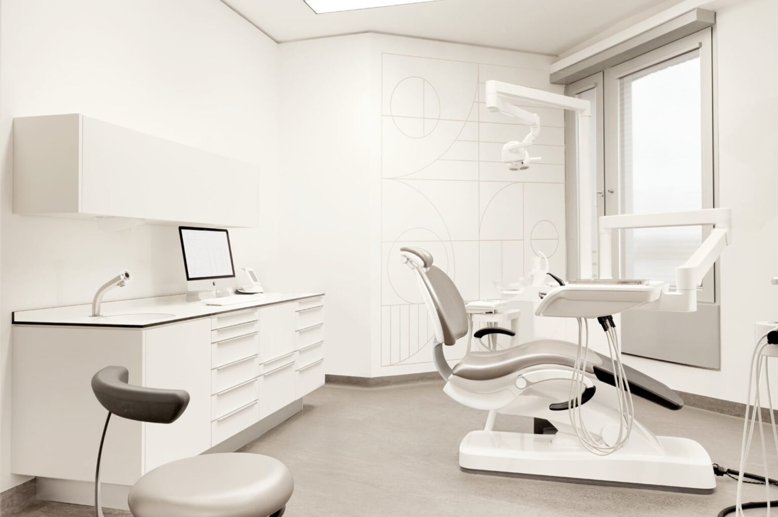 Zahnbehandlungsraum mit einem weißen Behandlungsstuhl, einem Computerarbeitsplatz und modernen zahnärztlichen Geräten.