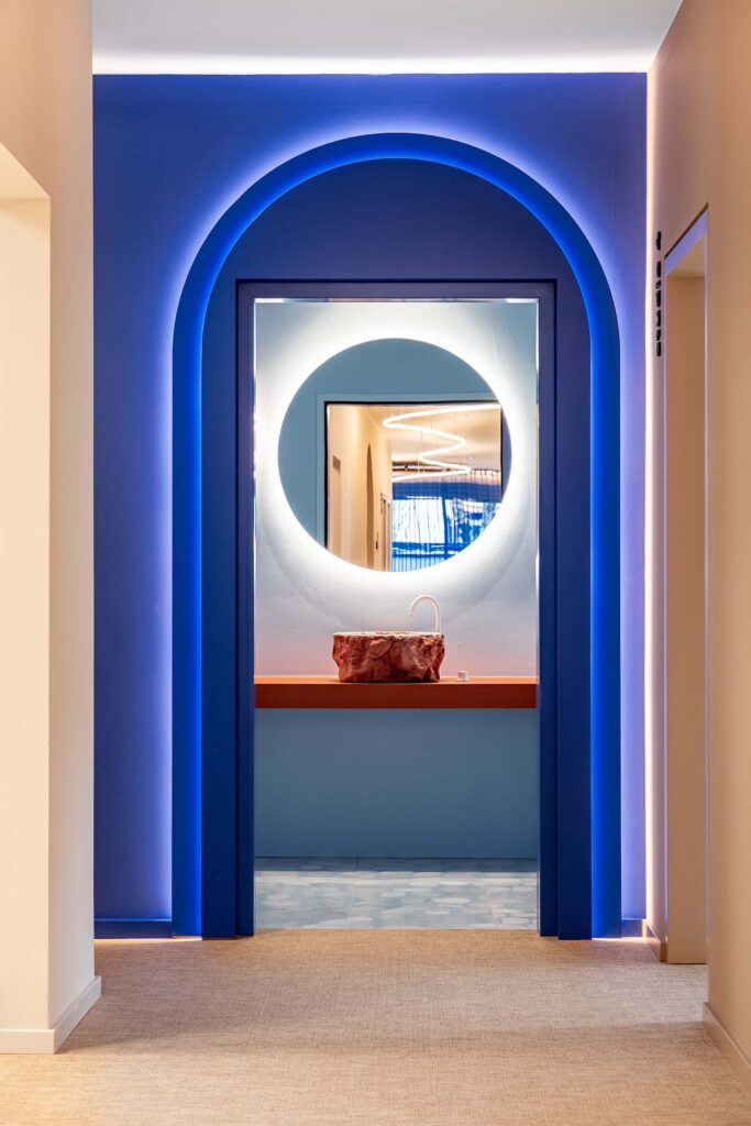 Im LIV*dental studio prägt ein blaues Lichtband das moderne Interieur: ein rundes Leuchtmotiv rahmt den Durchblick in den hellen Flur.