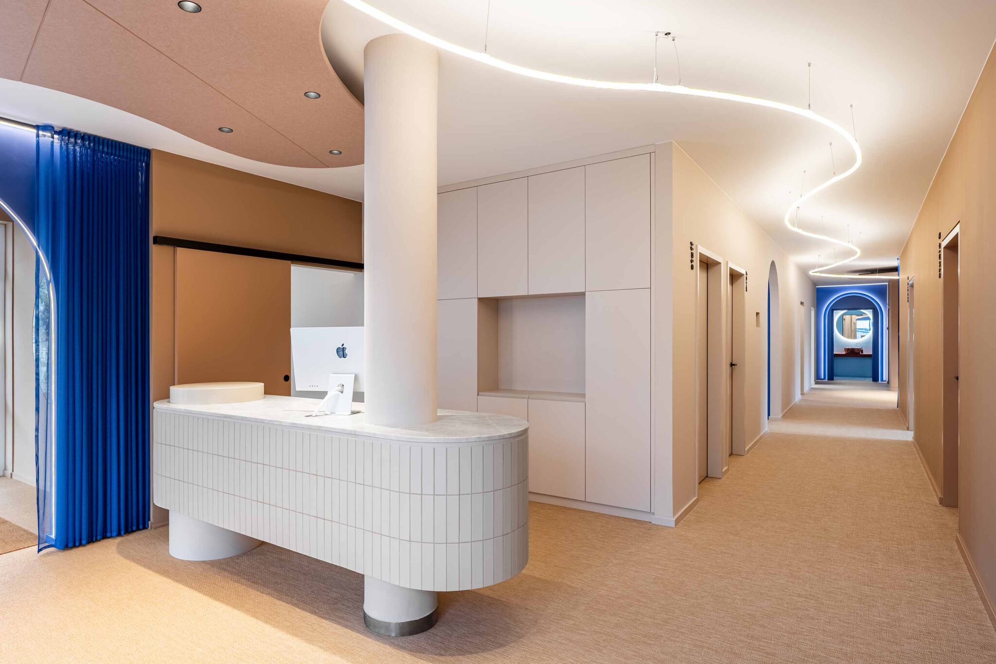 Heller Empfangsbereich im LIV*dental studio mit weißem Tresen, blauen Akzenten und indirektem LED-Licht – Zahnarzt Deisenhofen für ganzheitliche Zahnmedizin.