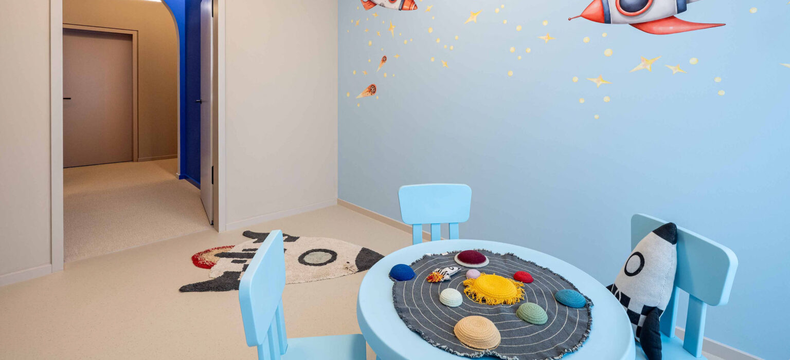 In der LIV*dental studio Praxis in Deisenhofen prägen helle Wände und eine hellblaue Kinder-Ecke den Raum, mit rundem Tisch, Teppich und Spielzeug.