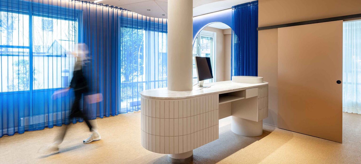 Lichtdurchflutete Praxis in Deisenhofen mit moderner Empfangstheke und blauen Vorhängen, klare Linien und hochwertige Materialien im LIV*dental studio.