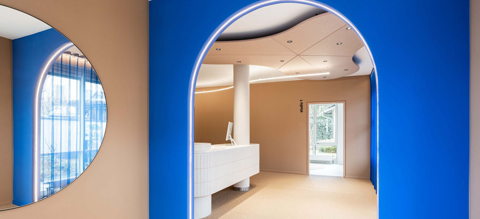 Moderne Praxis von LIV*dental studio mit lichtdurchfluteten Durchgängen, blauen Wandflächen und silbernen LED-Rahmen im hellen Warte- und Empfangsbereich.