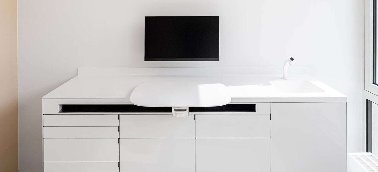 Helle, moderne Behandlungsbank mit weißen Schränken, schwarzem Bildschirm und klarer Armatur – LIV*dental studio LIV experience in ruhigem Design.