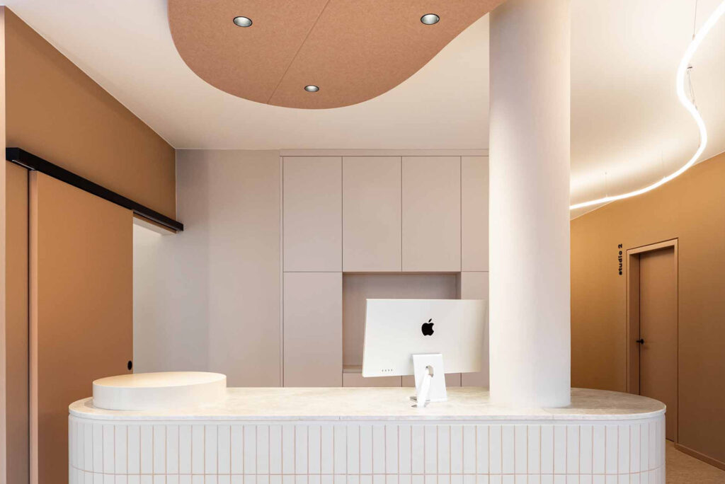 Modernes Empfangsambiente im LIV dental studio in Deisenhofen mit weißer Theke, beigen Wänden und dezentem LED-Lichtband im Raum.