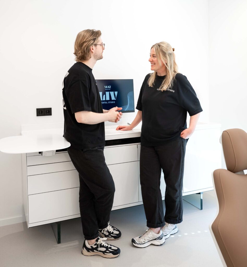 Zwei lächelnde Teammitglieder des LIV*dental studios begrüßen sich im Behandlungsraum mit einem Handschlag am Empfangstresen.