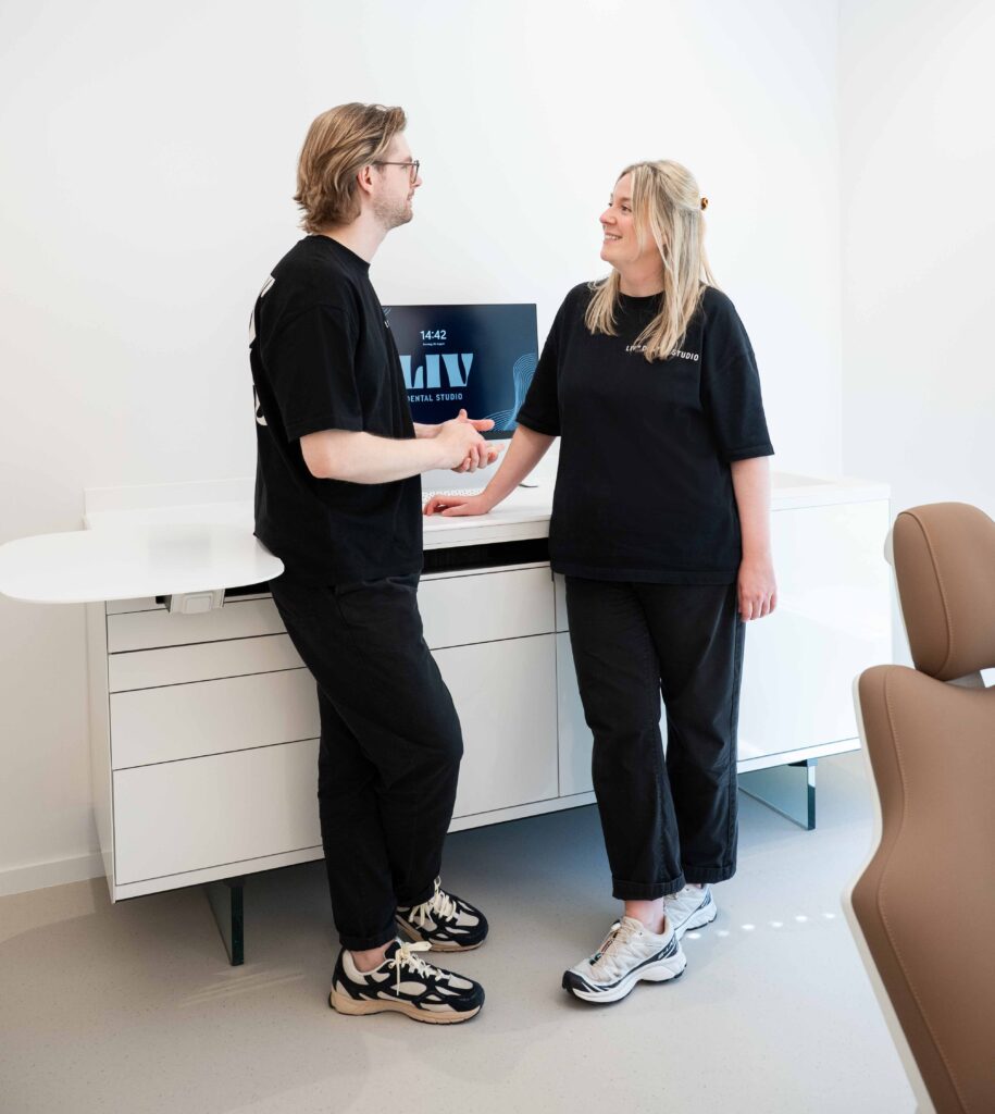 Zwei Mitarbeitende von LIV dental studio begrüßen sich in der Zahnarztpraxis in Oberhaching lächelnd per Handschlag.