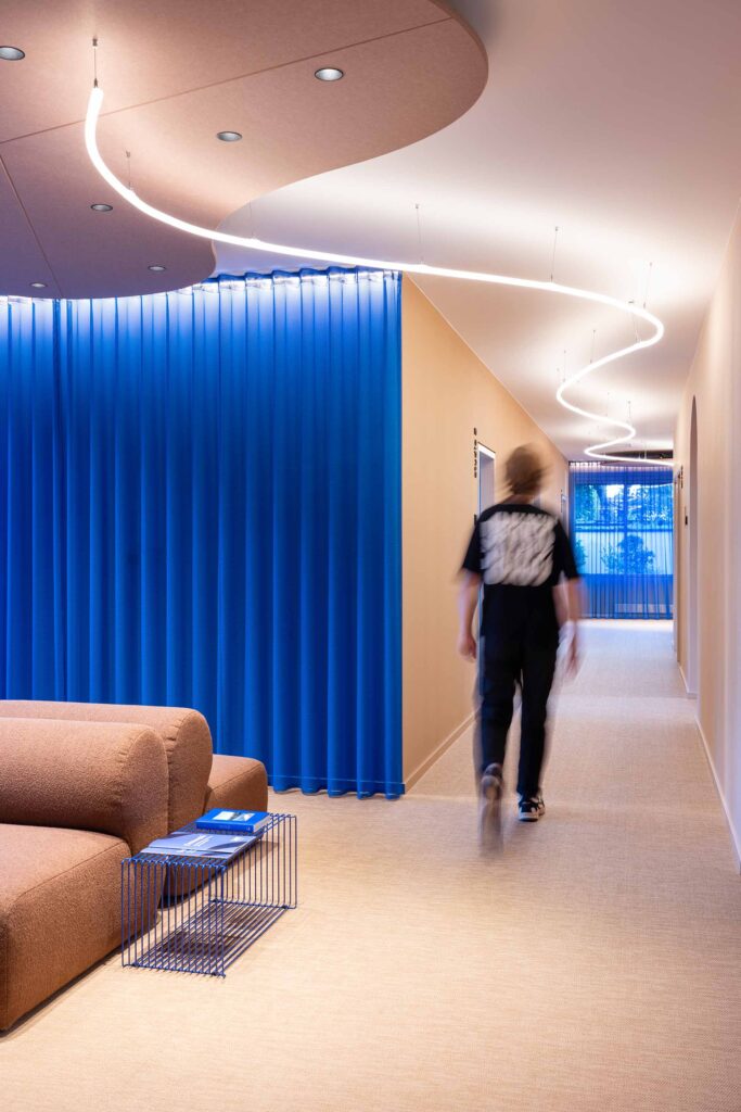 Ein Teammitglied geht durch den modernen Flur des LIV dental studio, vorbei an blauen Vorhängen und einem gemütlichen Wartebereich.